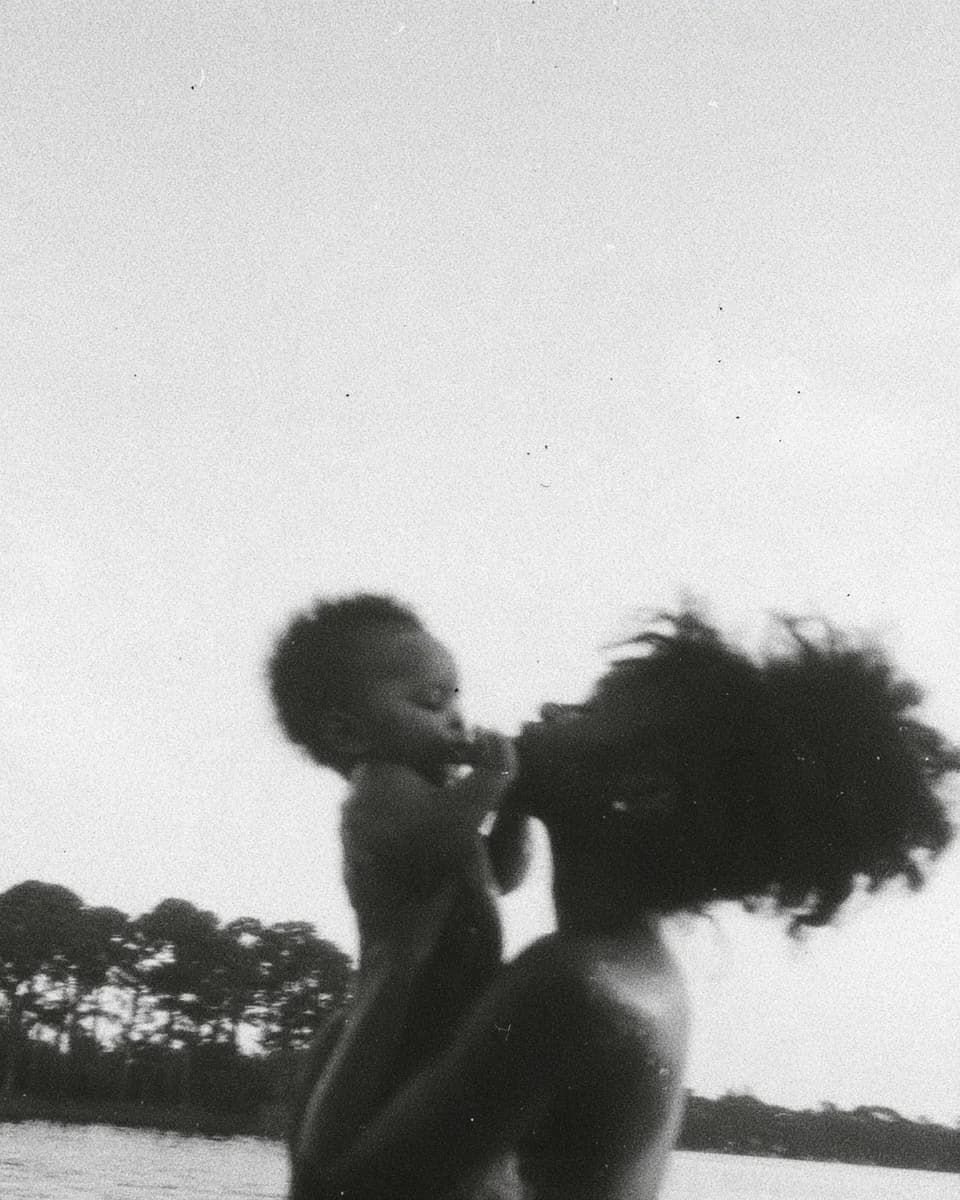 A mother lifting her baby to her face at the edge of a lake